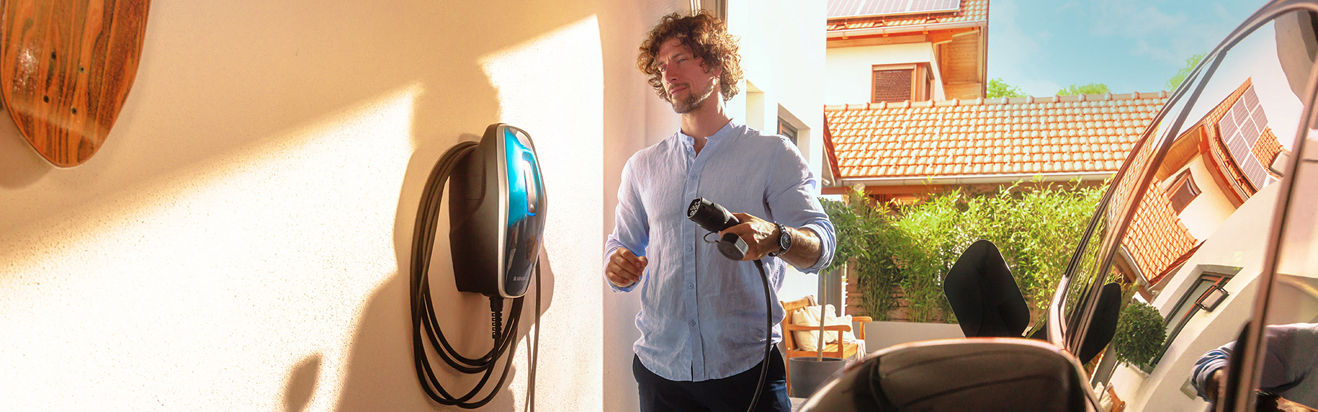 Mann steht in der Garage neben einer Wallbox und einem E-Auto 