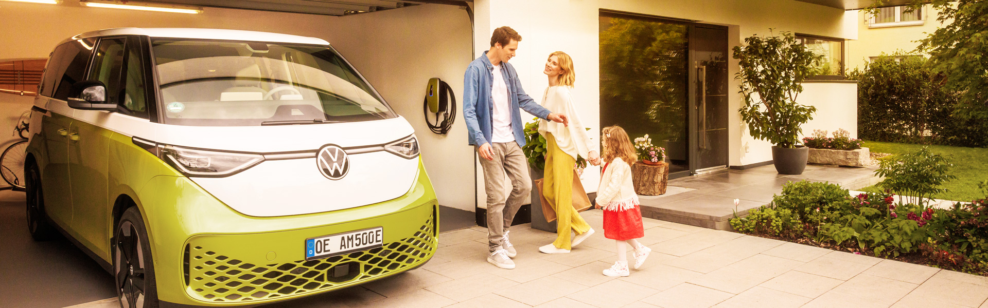 Familie vor einer Garage mit einem E-Auto und einer Wallbox