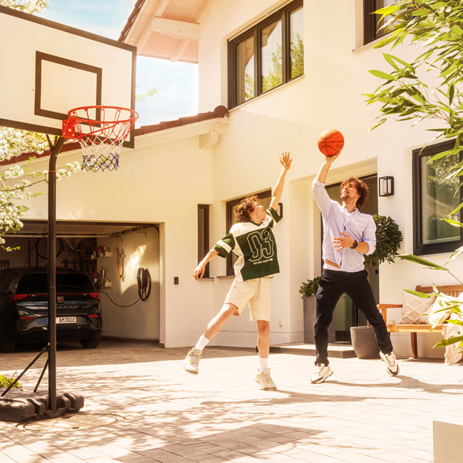 Mann spielt mit Sohn Basketball vor dem Haus