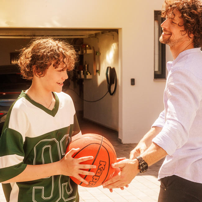 Vater spielt mit Sohn Basketball, im Hintergrund hängt in der Garage eine MENNEKES Wallbox 