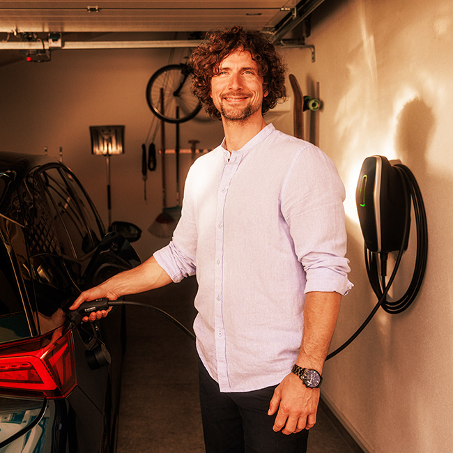 Mann steht in der Garage und lädt sein E-Auto