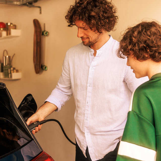 Vater lädt das E-Auto gerade auf. während der Sohn zuschaut