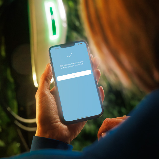 Frau verschickt Dienstwagenabrechnung am Smartphone im Hintergrund Wallbox AMTRON® 4You 500 