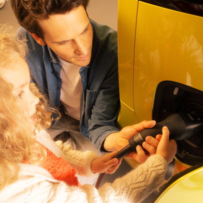 Ein Vater zeigt seiner kleinen Tochter, wie man ein Elektroauto lädt, indem sie gemeinsam den Ladestecker einstecken.