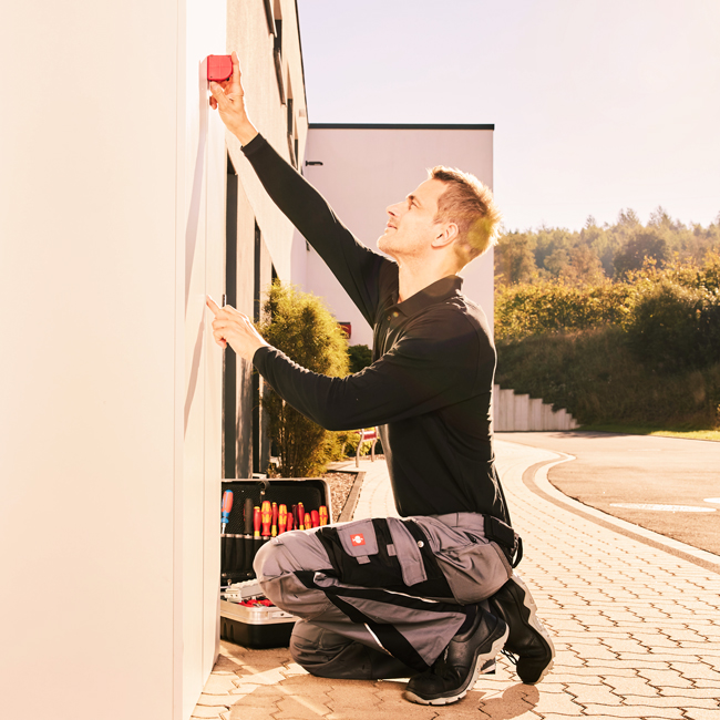 Installateur bereitet an einer Hauswand die Installation einer Wallbox vor