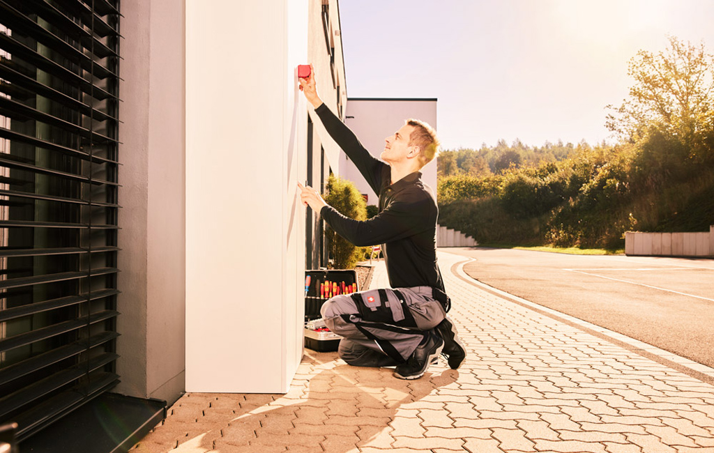 Installateur vor einer Hauswand, installiert eine Doppelwallbox