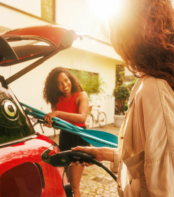 Zwei Freundinnen stehen neben einem E-Auto, während es geladen wird