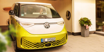 Familie fährt mit gelben E-Auto aus der Garage, daneben hängt eine AMTRON 4You 500 Wallbox in gelb.