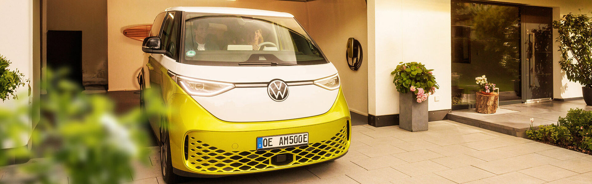 Familie fährt mit gelben E-Auto aus der Garage, daneben hängt eine AMTRON 4You 500 Wallbox in gelb.