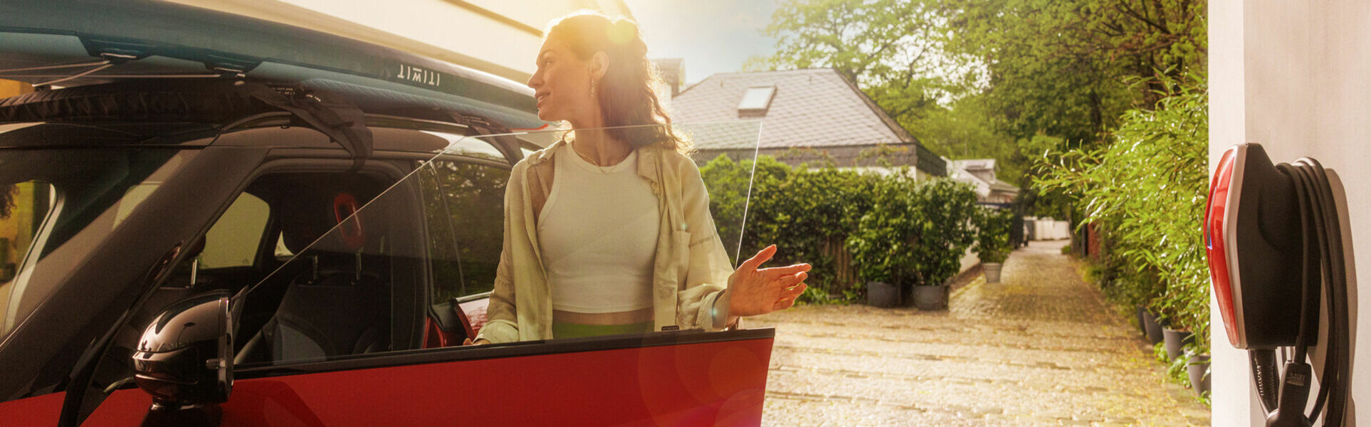 Frau steigt in ein rotes E-Auto ein, daneben hängt in der Garage die Wallbox AMTRON 4You 100 in rot