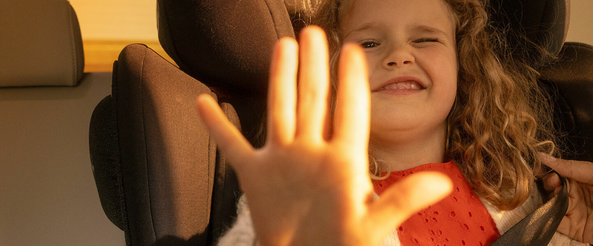 Kind sitzt im Auto und hält Hand in die Kamera